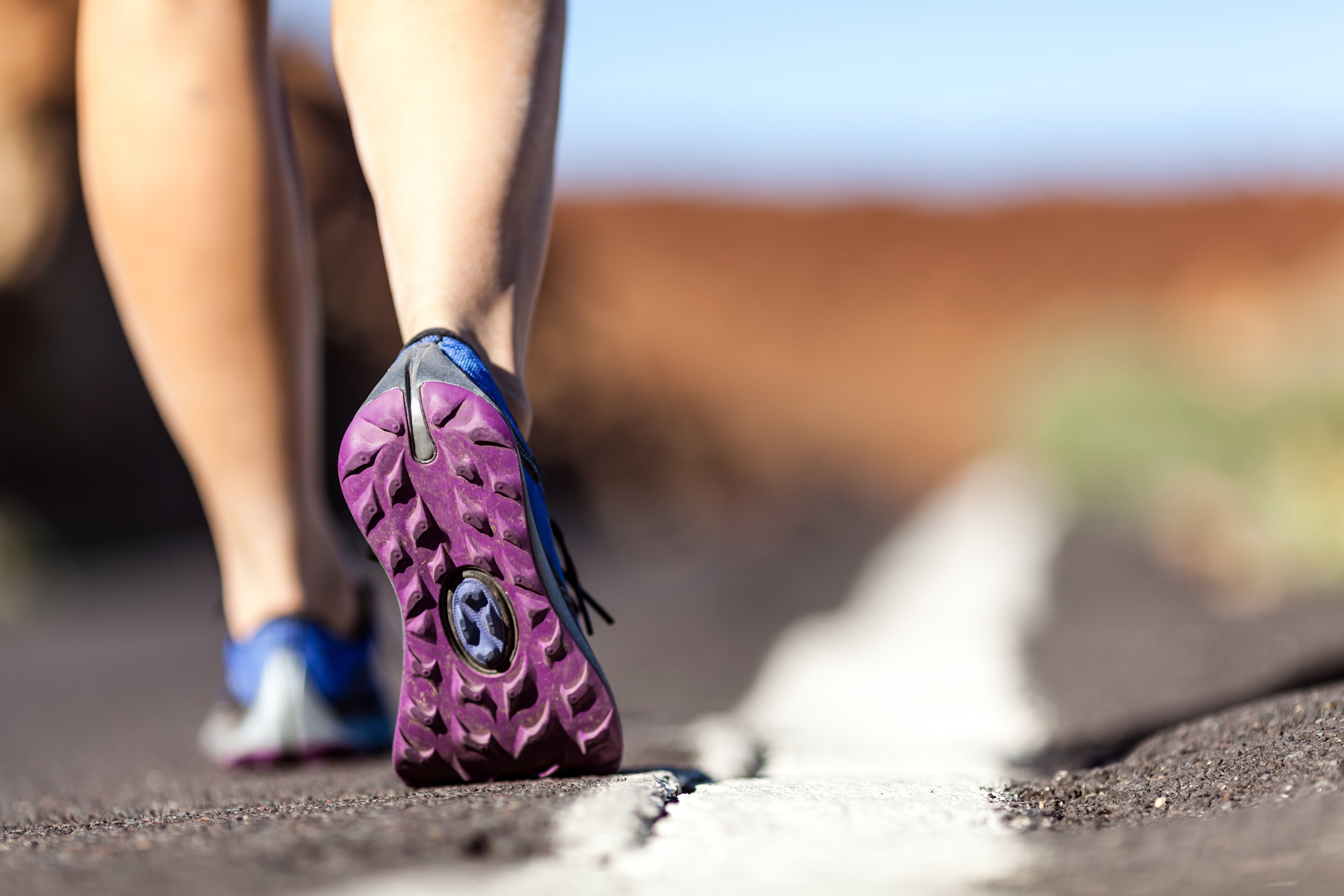 Walking or running legs on mountain road, adventure and exercising in summer nature. Female hiker or runner foot and sport shoes doing workout outdoors.